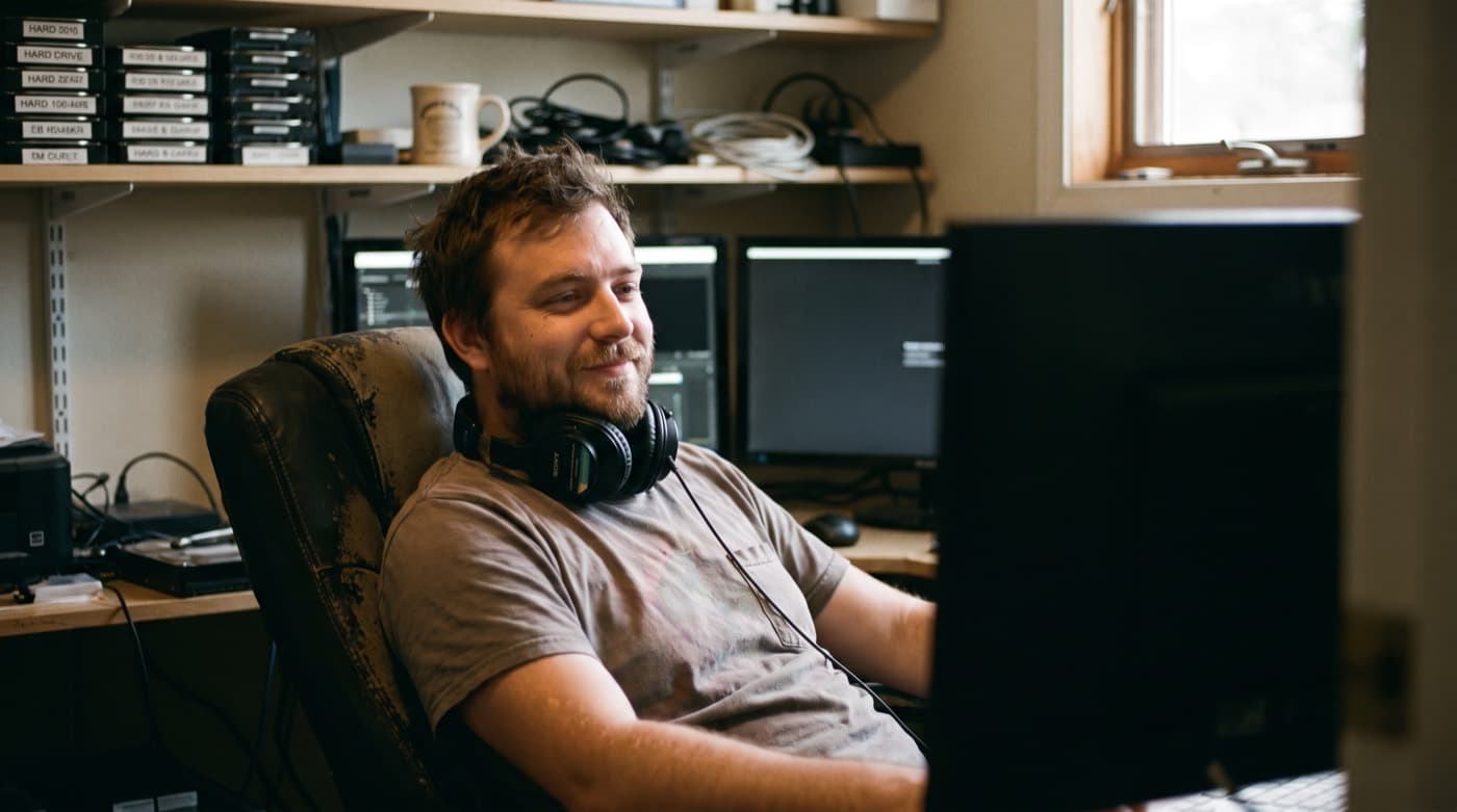 A video editor at the desk in a dimly lit edit suite